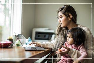 mum working from home on laptop while holding young child