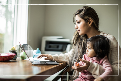 mum working from home on laptop while holding young child