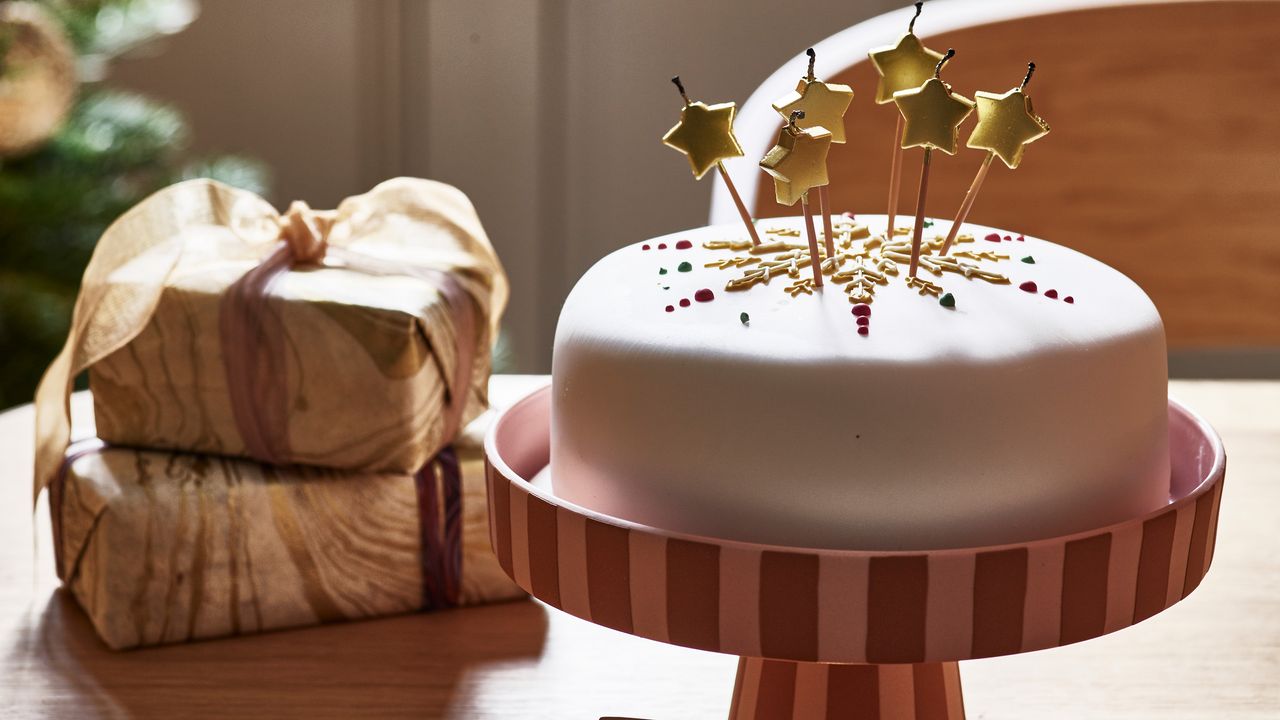 Christmas gifts for foodies Christmas cake with star sparklers on a stripy cake stand beside two wrapped gifts 