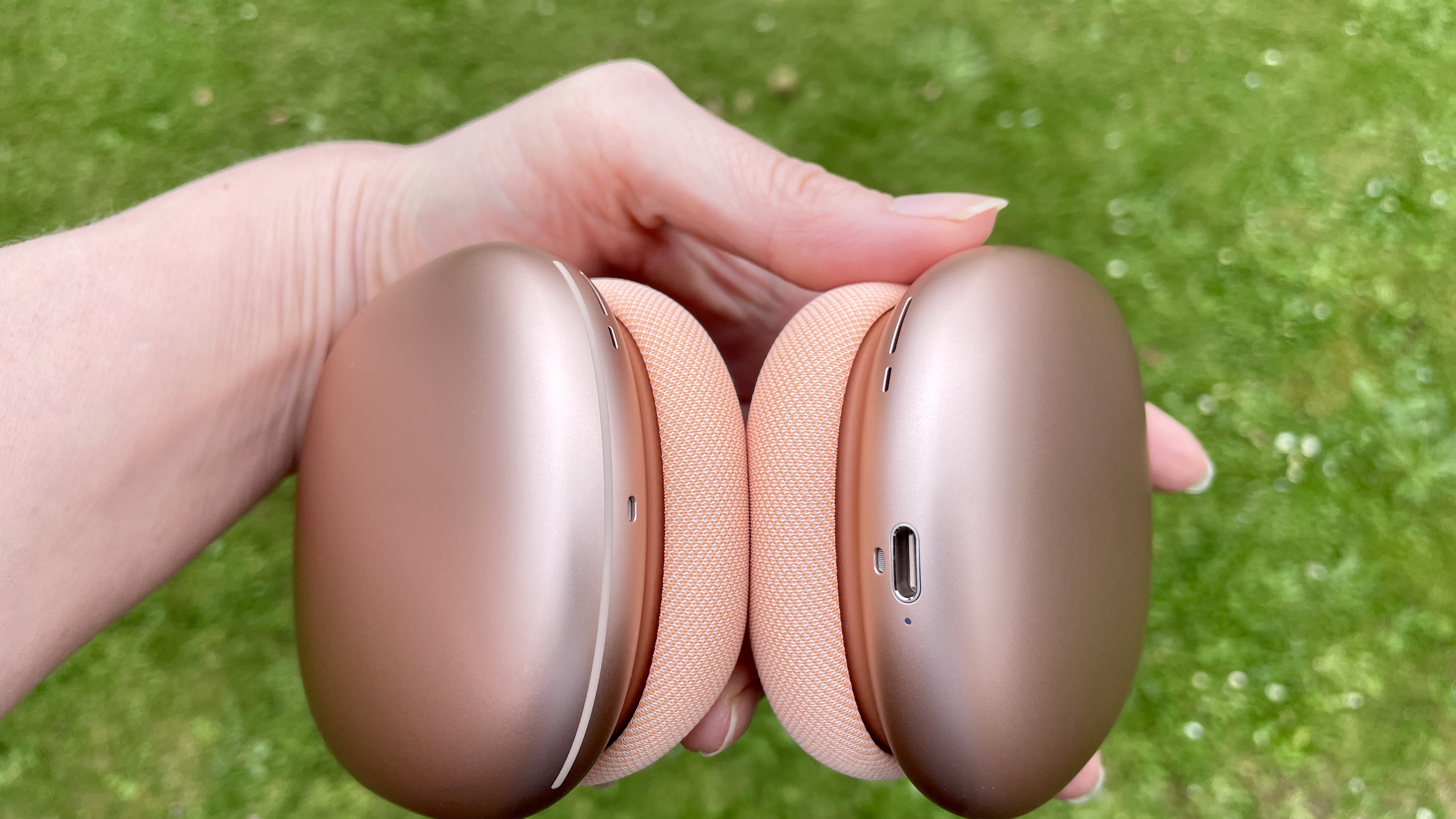 AirPods Max 2 in a garden, held in a hand, in close-up to show the ear cups and band