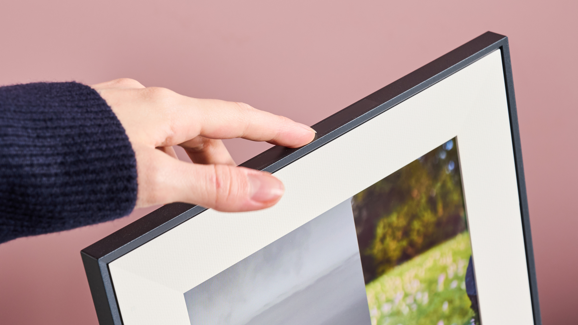A hand swiping the touchbar on the top of the Aura Aspen, showing the photos on screen sliding from one to the next.
