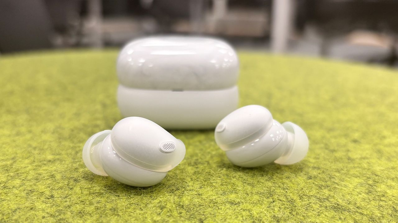 A white pair of Sony LinkBuds Fit in-ear headphones, sitting on an artificial grass surface. The white charging case is visible behind them.