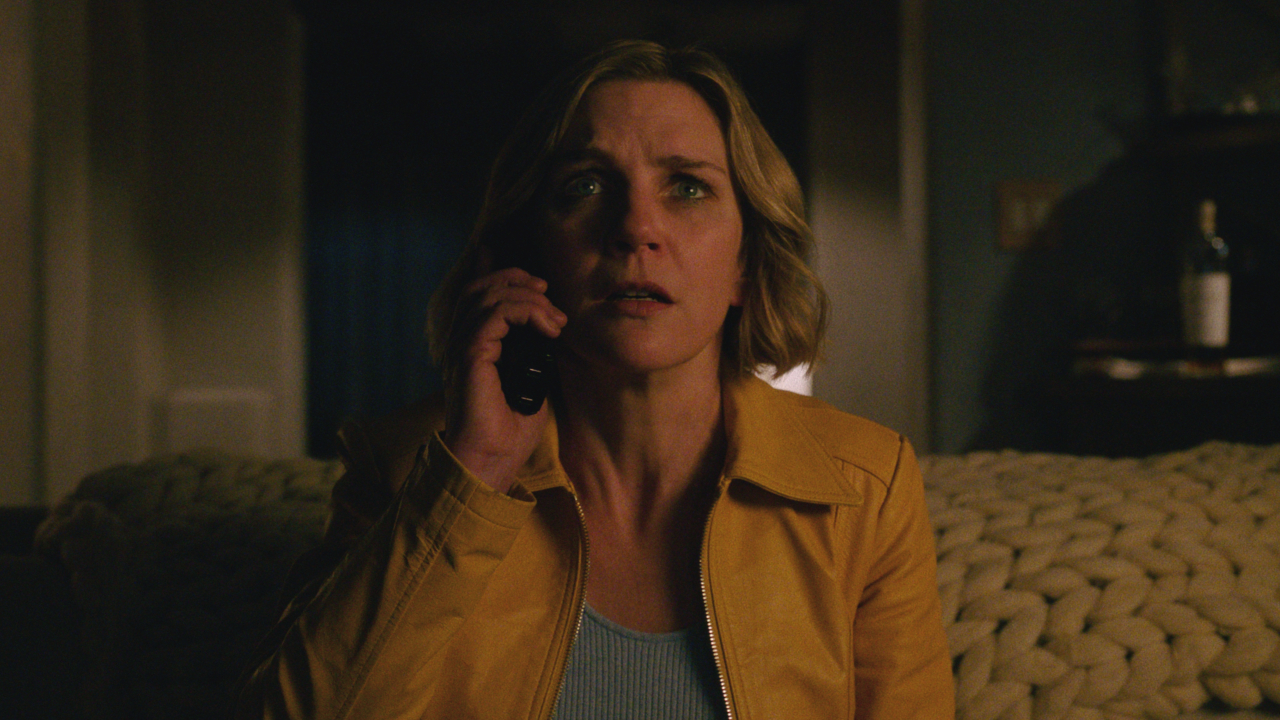 Rhea Seehorn sits shocked while taking a phone call in Pluribus S1 E1.