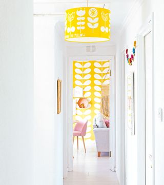 White hallway with yellow pendant and matching wallpaper in living room beyond hallway