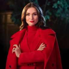 Sophie Ellis-Bextor wearing red coat, suit, and jumper with tree behind her