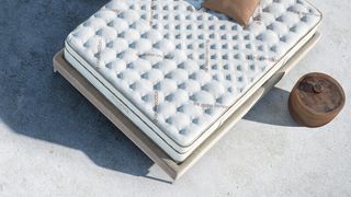 Memory foam vs hybrid mattress: the Saatva Classic shown on a beige fabric bed frame placed outside on a sunny day