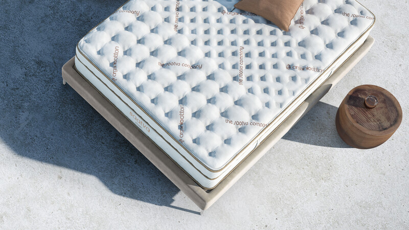 The Saatva Classic mattress photographed on a beige fabric bed frame placed outdoors on a sunny day