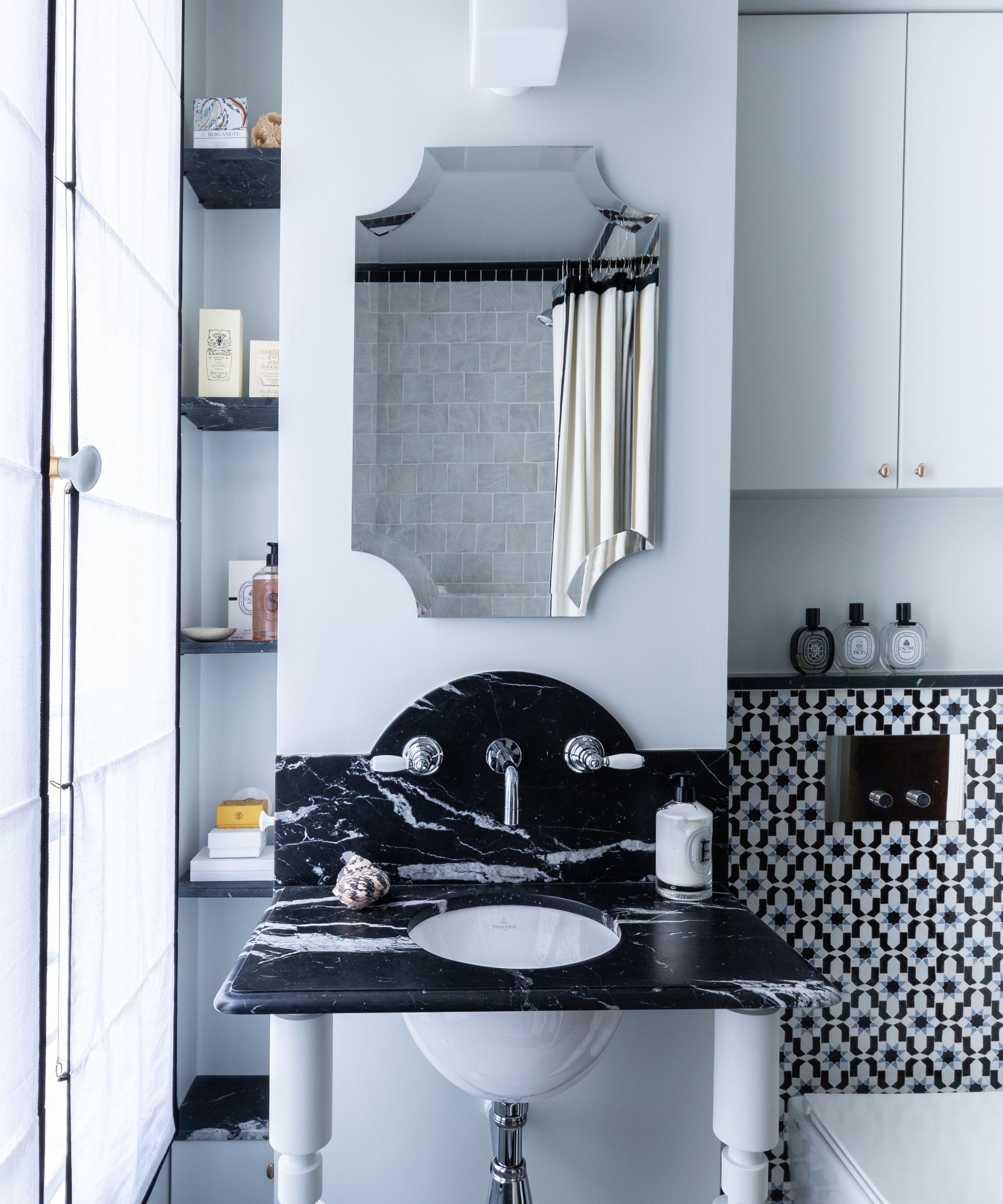 Bathroom with pale blue walls, black and white tiles, black marble sink and vintage mirror