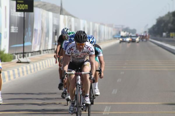 An escape crosses the finish line as the peloton looms in the distance