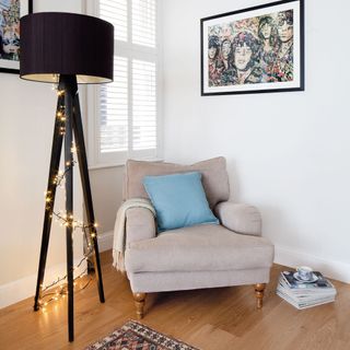 White office lounge area, beige armchair with pale blue cushion, floor lamp with fairy light decoration, colourful framed artwork