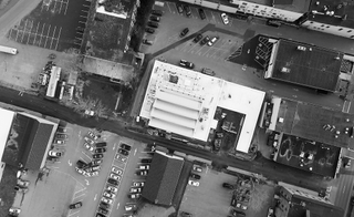 An aerial view of a factory complex with various sized buildings and cars parked next to them.