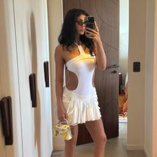 Kylie Jenner wears a white one-piece bathing suit, a mini white skirt, and flip flop heels.