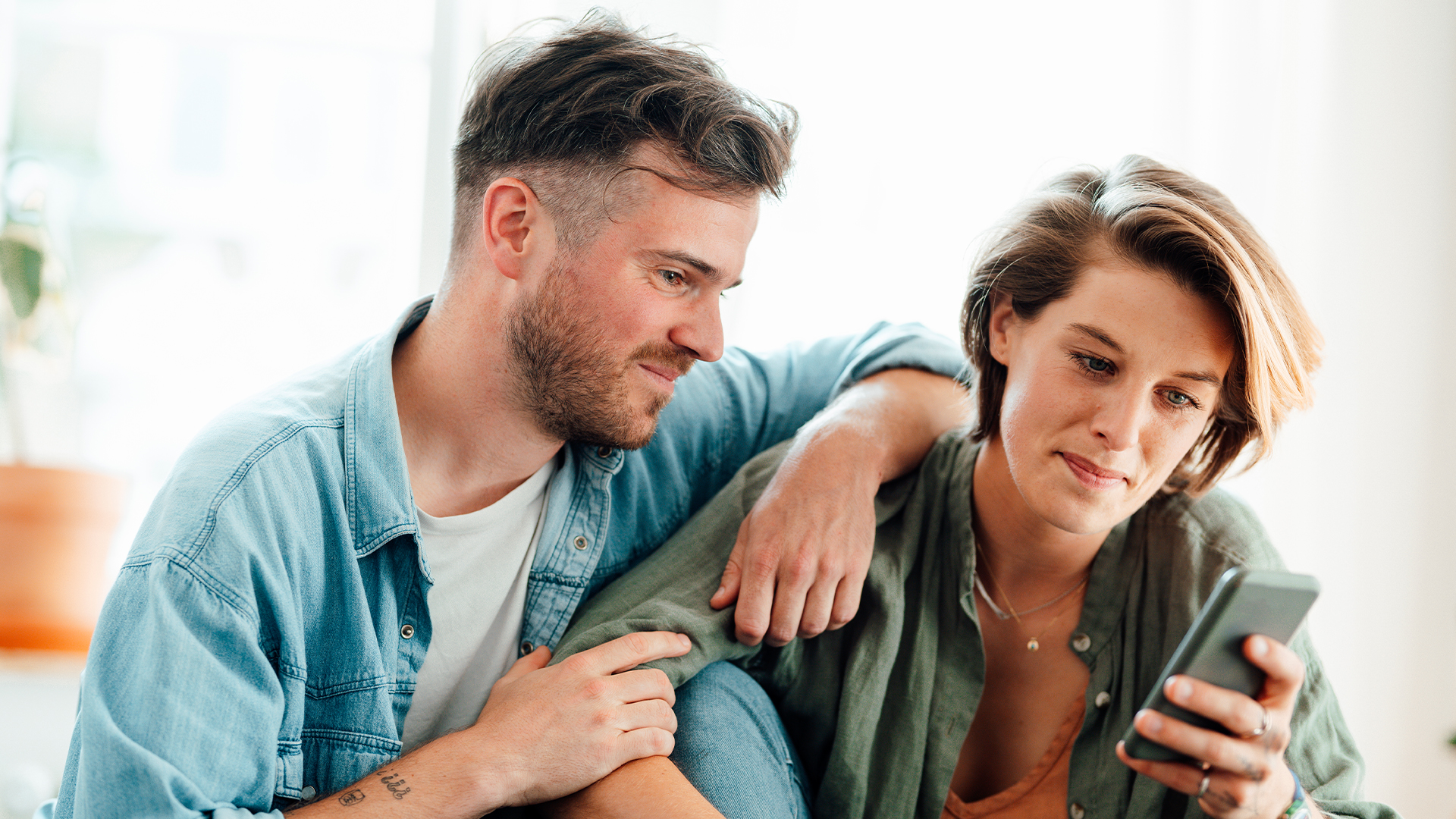 A man and a woman sit close together, looking at the same phone