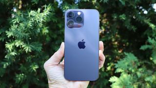 En hand som håller upp en blå Apple iPhone 14 Pro Max utomhus med baksidan vänd mot kameran.