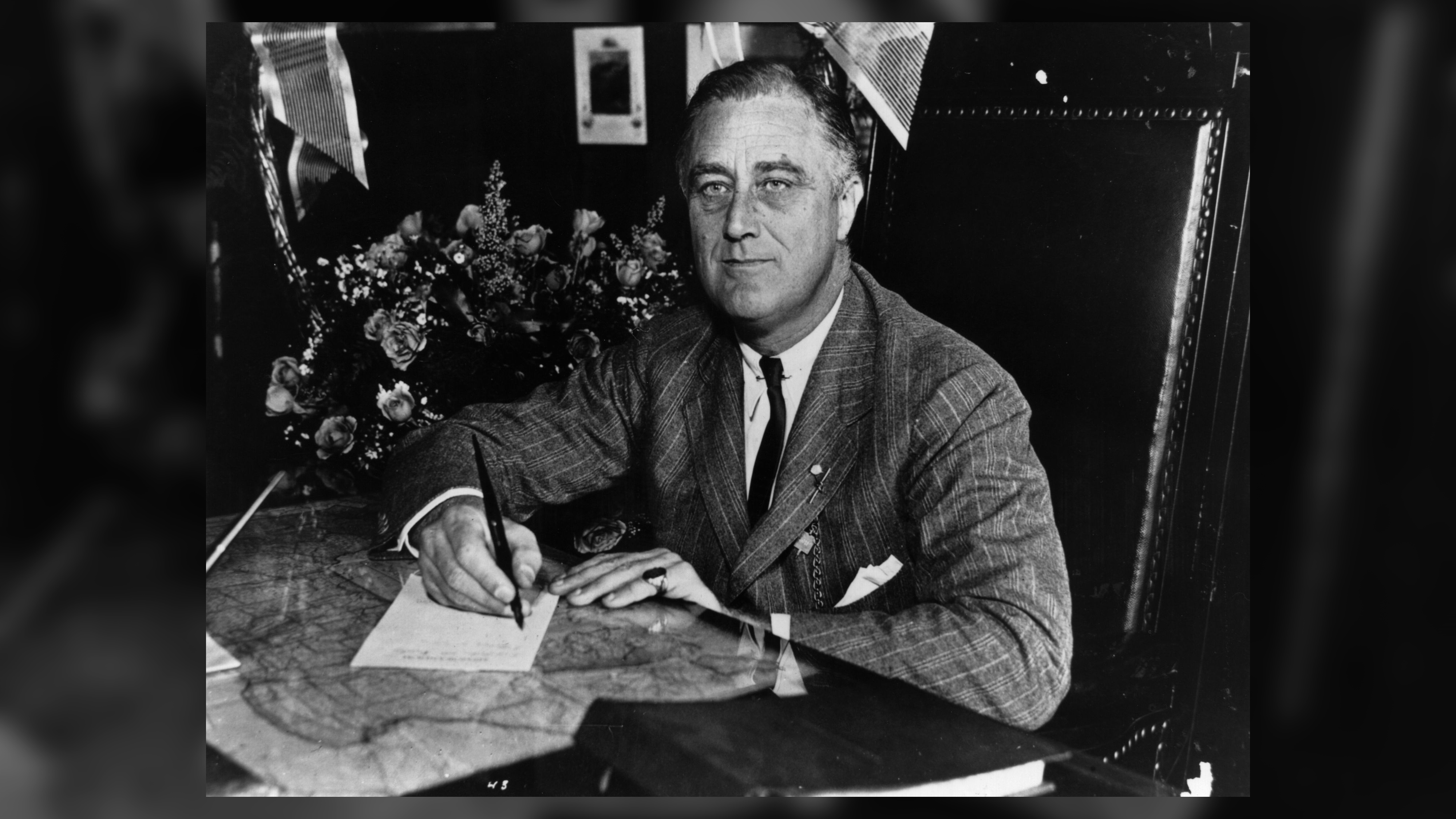 Black and white image of FDR signing a document at a desk
