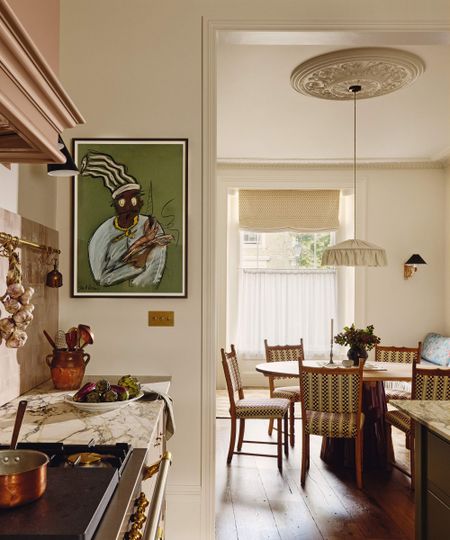 View from a marble-topped kitchen counter toward a dining area featuring a round wooden table, checkered chairs, and a large piece of art depicting a chef