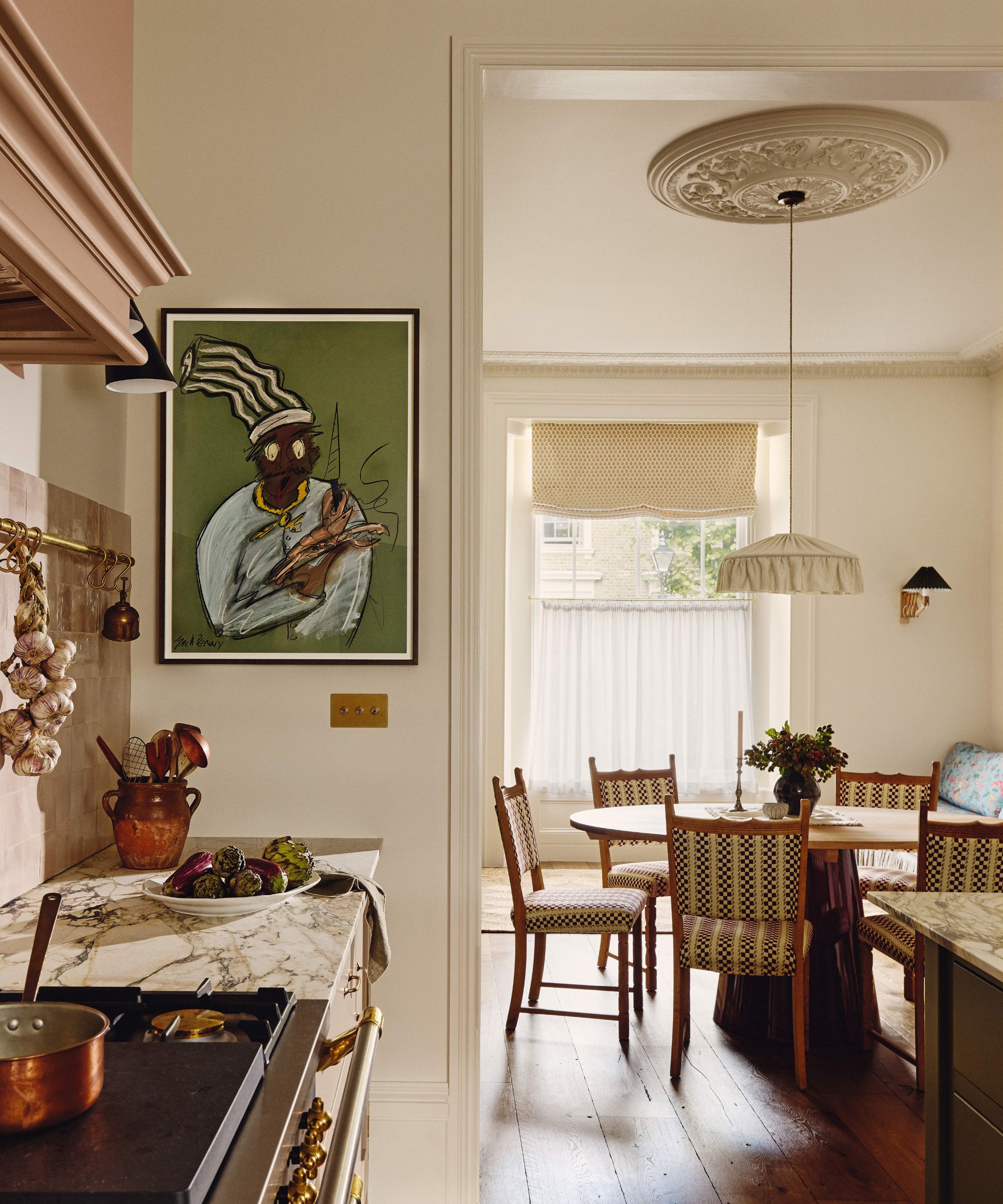 View from a marble-topped kitchen counter toward a dining area featuring a round wooden table, checkered chairs, and a large piece of art depicting a chef