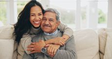 A smiling father is hugged by his adult daughter.