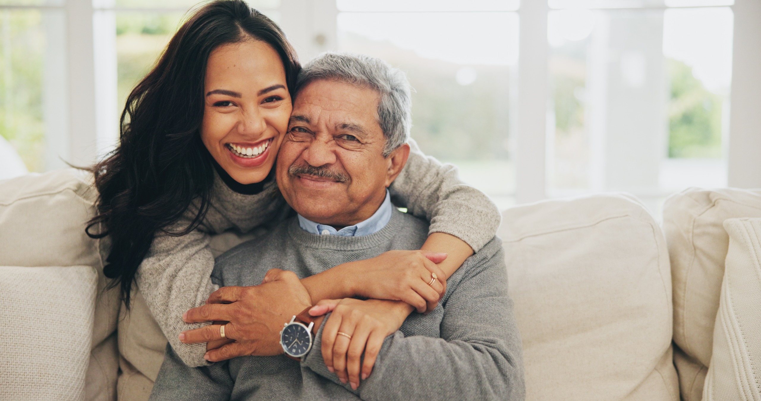A smiling father is hugged by his adult daughter.