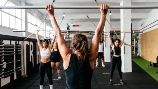 Woman in exercise class perform the overhead press shoulder exercise with barbells