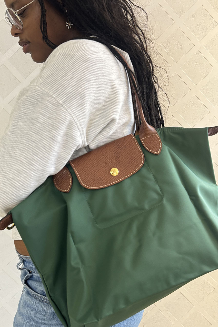 A woman wearing a grey hoodie, blue jeans, and a green canvas tote bag