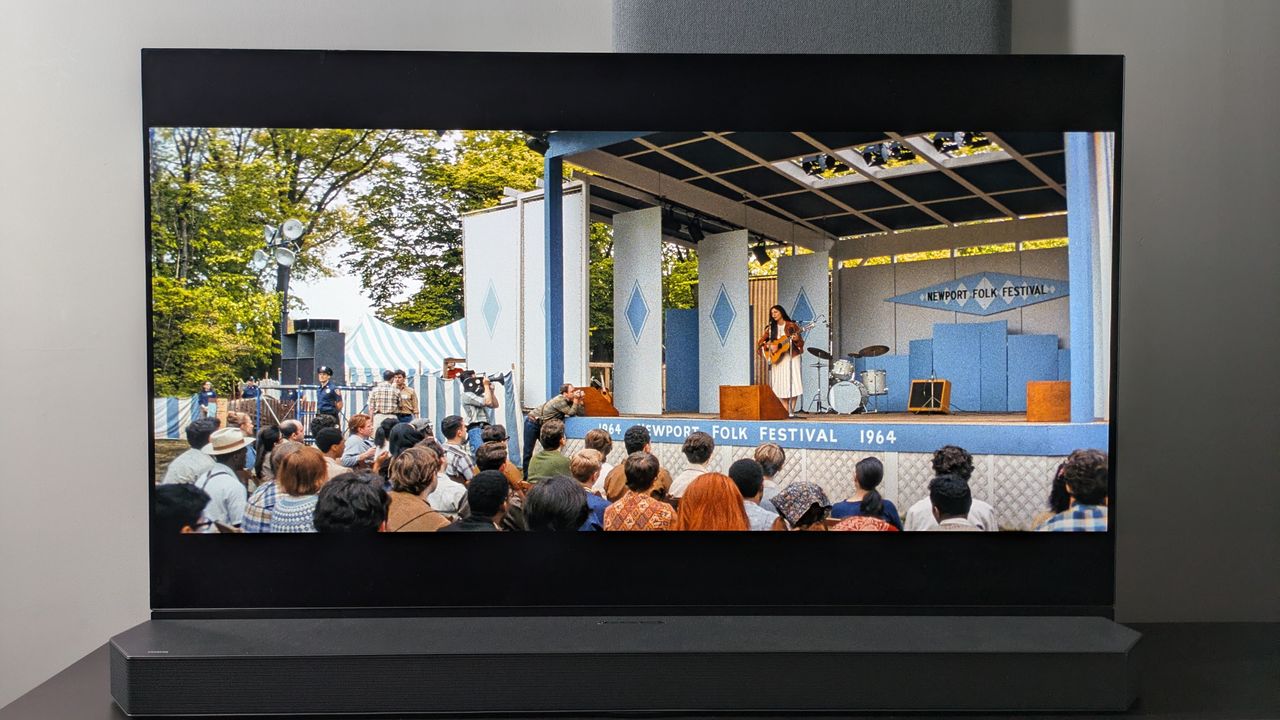 Panasonic OLED showing scene from A Complete Unknown with Monica Barbaro as Joan Baez singing on stage