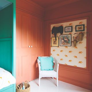 A colour-drenched terracotta-painted children's room with an elephant-print wallpaper panel