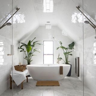 a white wet room with two shower heads and a white tub at the center surrounded by greenery