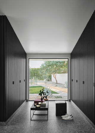 A dressing room with floor to ceiling windows looking out onto a backyard with cacti and trees