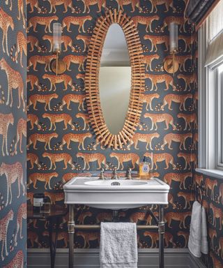 A powder room with an oval mirror and bright orange and blue wallpaper with tigers