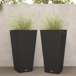 two tall black planters with ornamental grasses growing in them on a wooden decking