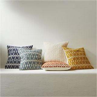 Five pillows with colorful fronts with leaf patterns on them, white backs. On a white platform