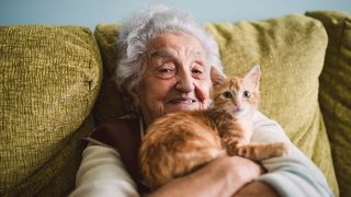 senior woman sitting on couch holding ginger kitten