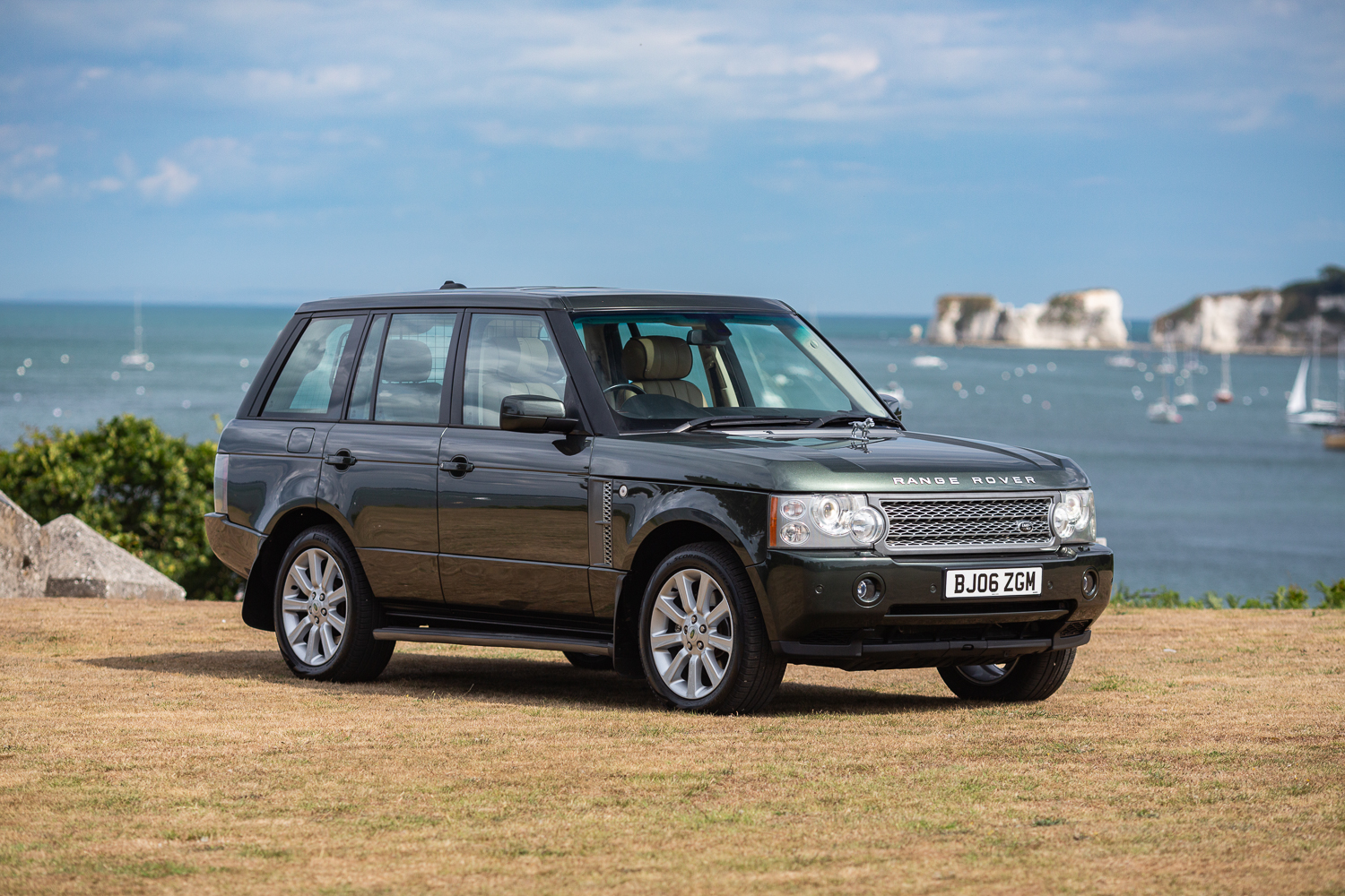 A Range Rover sitting next to the sea with sailboats in the background