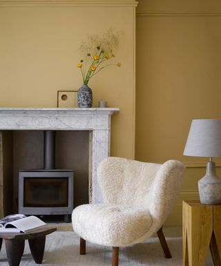 Yellow walls with comfy sheepskin armchair, and marble mantelpiece.