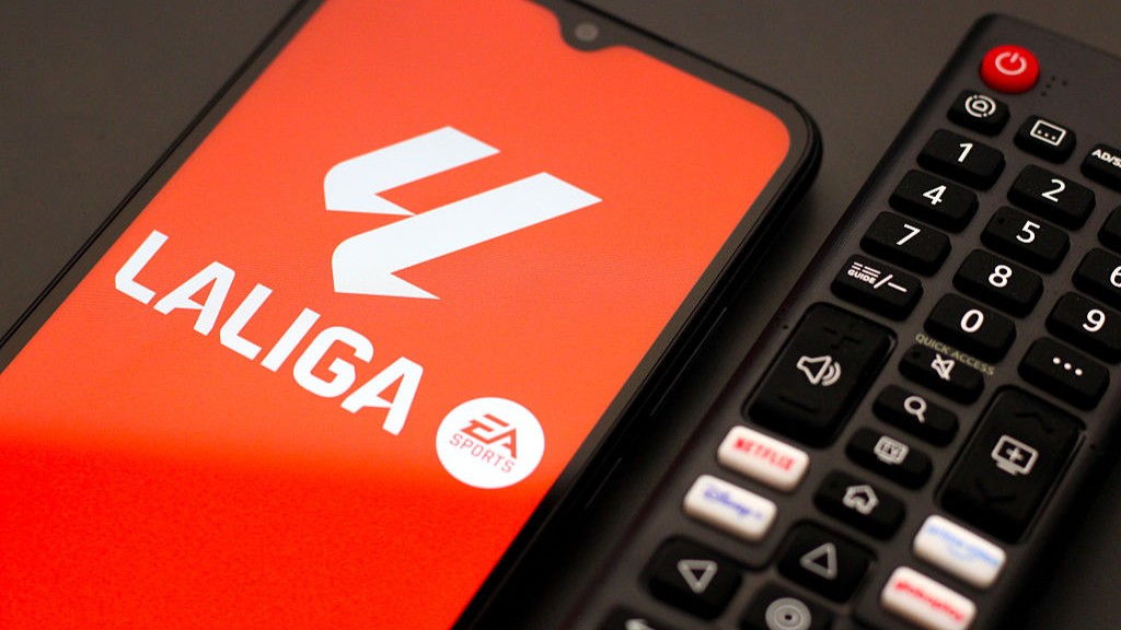 In this photo illustration, the La Liga logo is seen displayed on a smartphone screen next to a TV remote control.