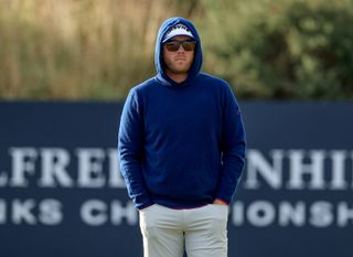 Talor Gooch walks down the fairway whilst wearing a blue hoodie