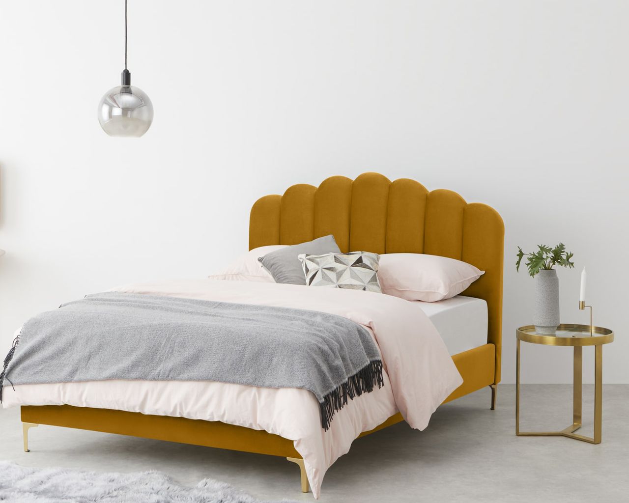 Made sale: yellow bed with scalloped headboard in bedroom with light pink bedding, gold bedside table and grey blanket and vase