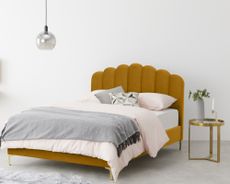 Made sale: yellow bed with scalloped headboard in bedroom with light pink bedding, gold bedside table and grey blanket and vase