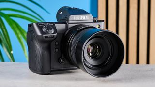 The Fujifilm GFX100 II on a stone surface with a blue wall in the background