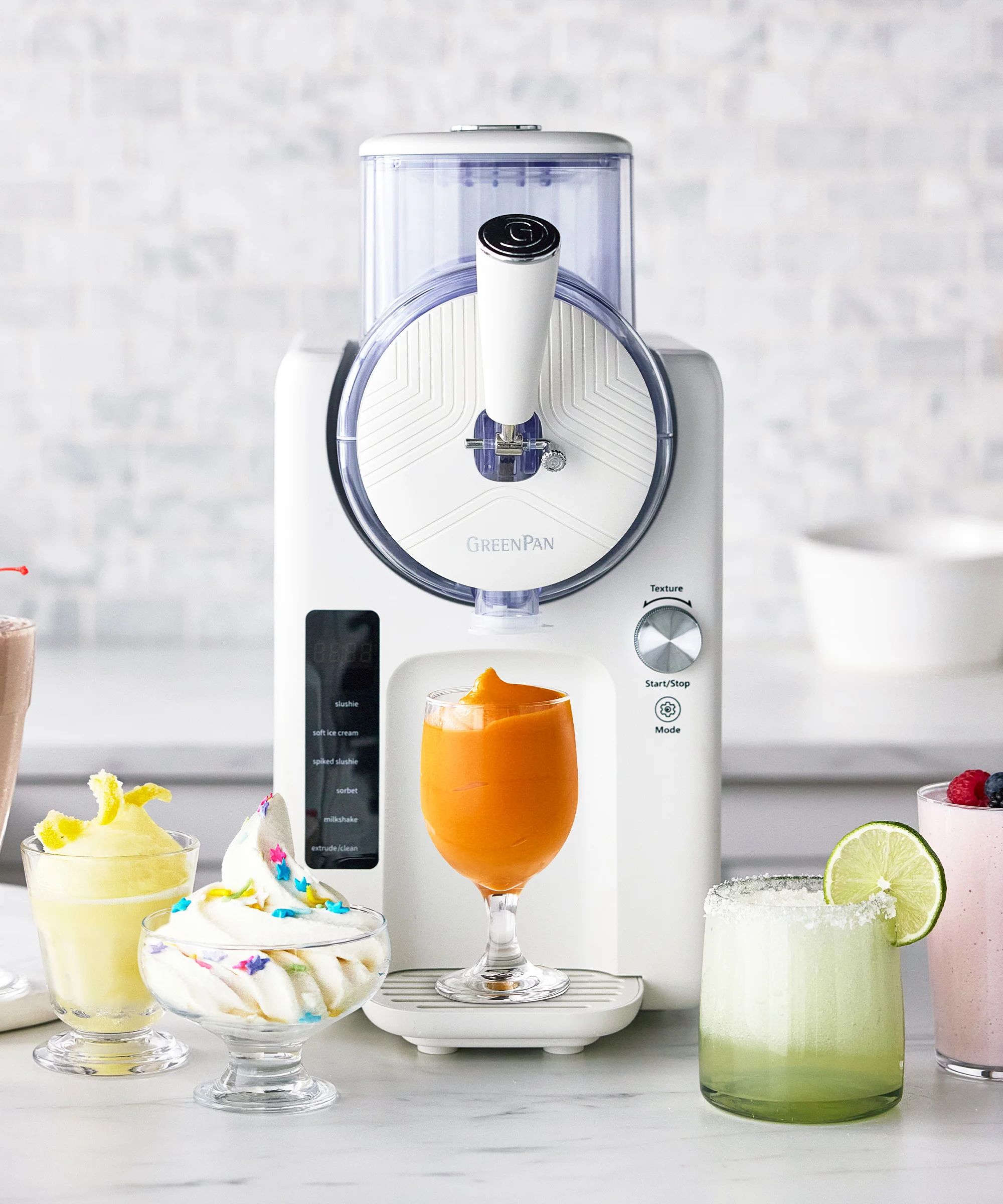 White ice cream maker with fountain handle, with an orange frozen drink, two frozen cocktails and a dish of soft-serve in front of it