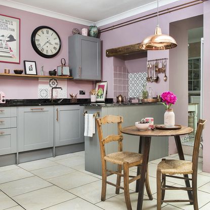 kitchen area with pink wall and grey kitchen units and round table and chair and tiles flooring