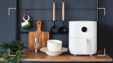 a dark grey kitchen with wooden counter with a white air fryer and utensils to show the best air fryer accessories for cooking