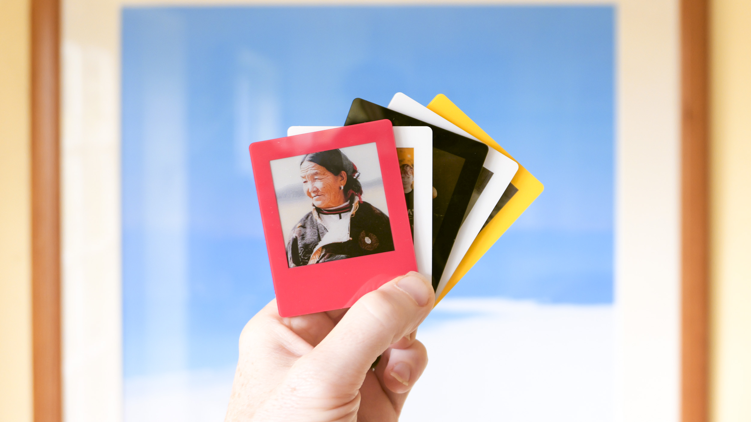 Five Vidabay Snap E Ink Polaroid-like frames in the hand, of the four color varieties, held in front of a framed picture
