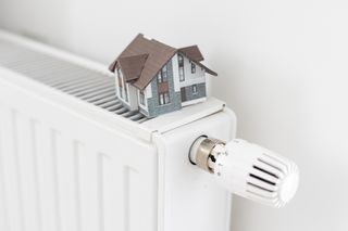 A close up of a white radiator indoors, with a small model house sitting on top.