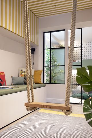 swing hanging in a playroom from a yellow and white striped ceiling
