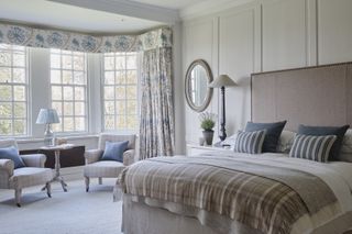 An example of how to design a bedroom showing a neutral bedroom with a double bed, an upholstered headboard, a seating area and lamps