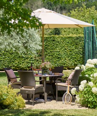 Rattan outdoor dining set with table and chairs and a parasol in a garden scene