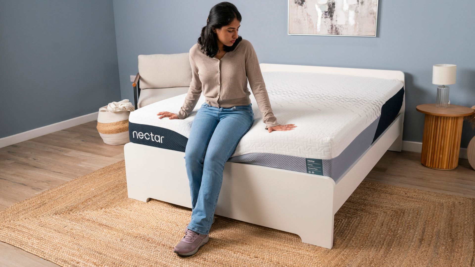 Tester Becky George sits on the foot of the Nectar Premier Memory Foam Mattress to test its sturdiness and support.