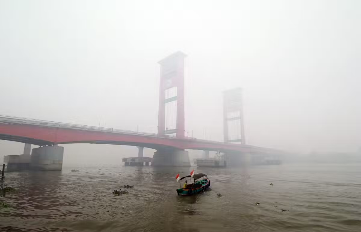a boat passes under a bridge with heavy haze in the sky